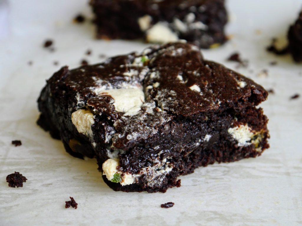 Three brownies are arrayed on a sheet of parchment with a scattering of crumbs between them.