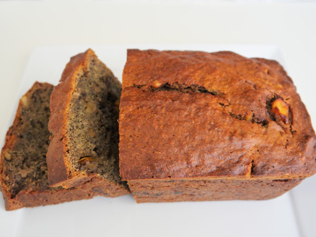 A loaf of golden brown bread with two cut slices falling from the left side rests on a white plate against a white background.