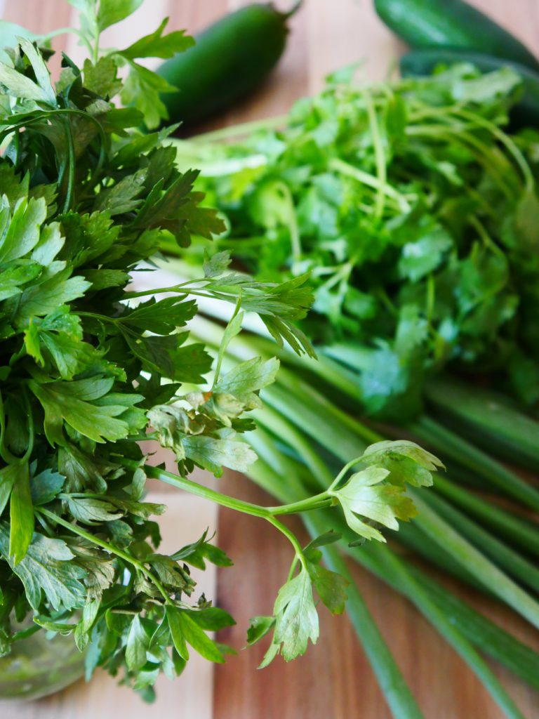 Parsley, cilantro, green onions, and jalapenos on a wooden cutting board.